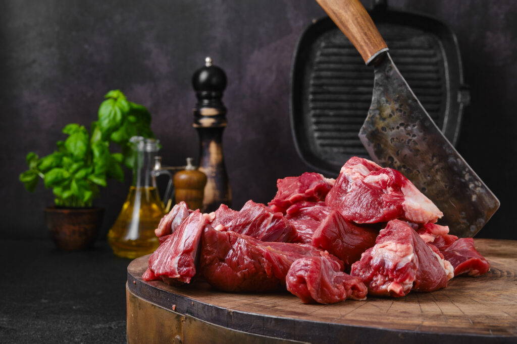 Chopping fresh beef meat for goulash or stew on wooden chopping stump